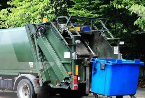 A green collection truck beside a blue recycling bin